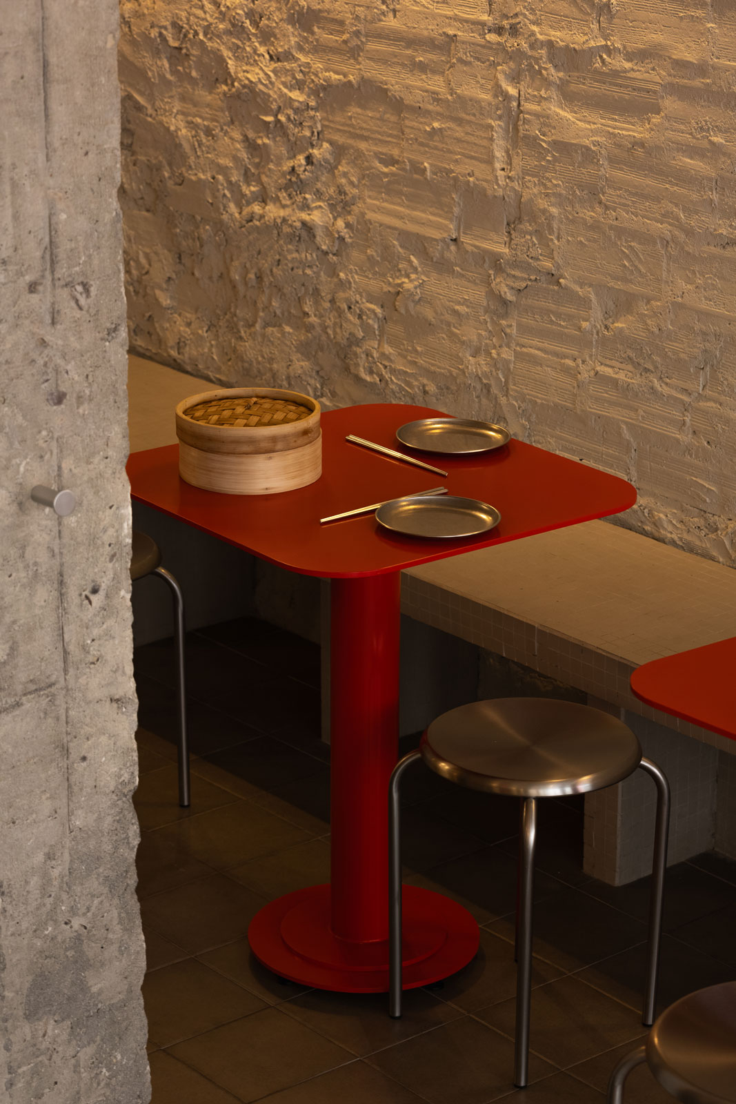 A red table with a bamboo steamer of dumplings.